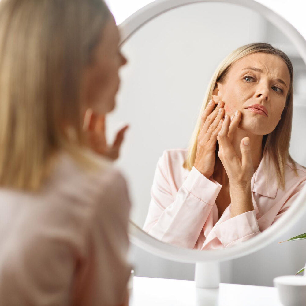 Woman in her 30s examining hormonal acne in the mirror during a skincare routine