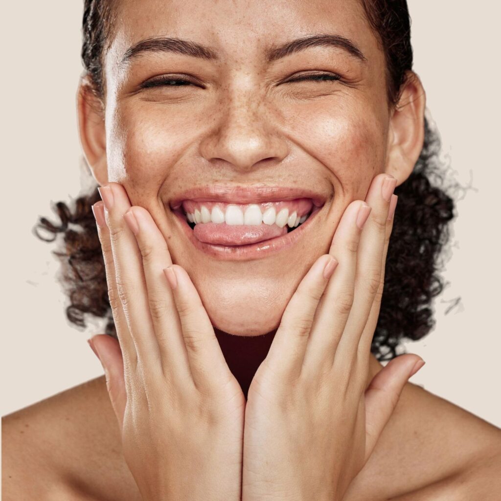Woman with clear skin smiling and touching her face, representing healthy skincare routine
