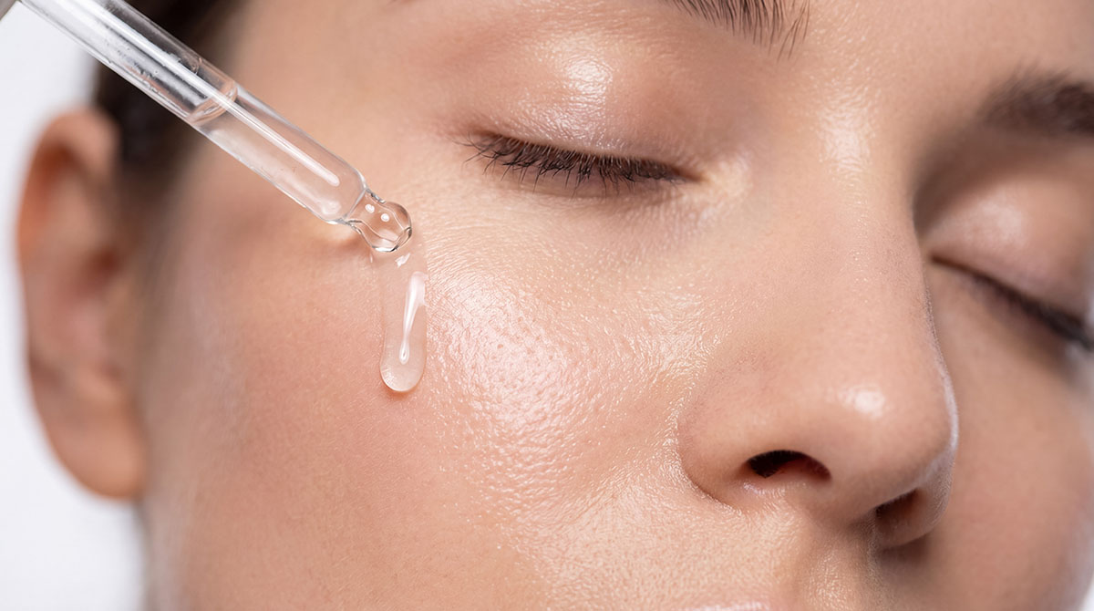 Close-up of a serum dropper applying anti-aging treatment to clear skin, representing anti-aging ingredients for acne-prone skin