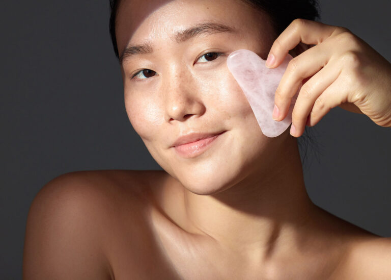 Woman using a rose quartz gua sha tool along her cheek for sagging skin